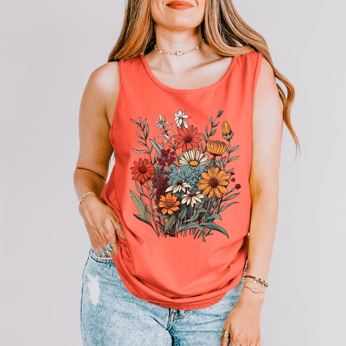 The Faithful Familiar vintage wildflower graphic tank top in coral, worn by a woman with light denim jeans.