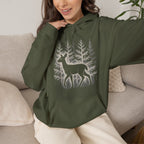 The Faithful Familiar olive green pullover hoodie featuring a white deer and forest graphic, worn by a smiling woman.