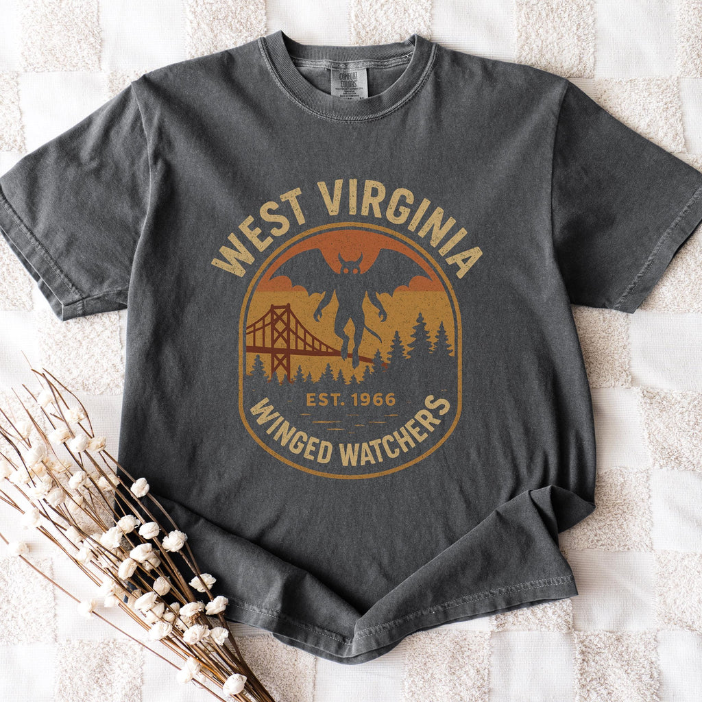 The Faithful Familiar charcoal grey Comfort Colors t-shirt with a vintage Mothman badge graphic in mustard and rust.