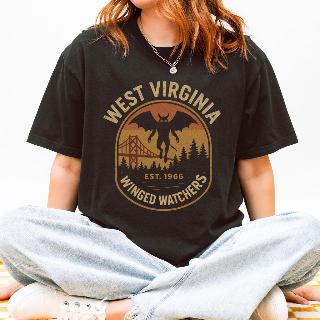 The Faithful Familiar black Comfort Colors t-shirt with a vintage Mothman graphic in mustard and rust colors.