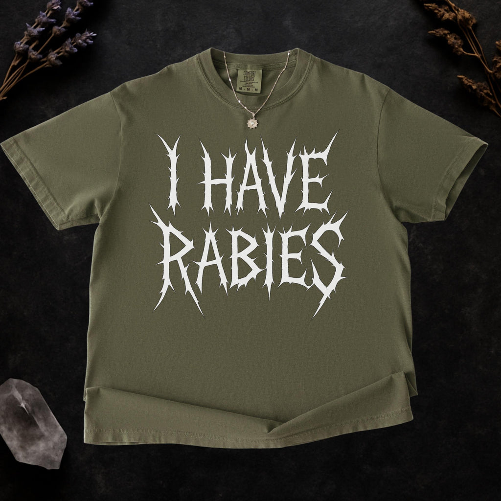 The Faithful Familiar olive green Comfort Colors graphic tee with white spiky metal-style text reading I HAVE RABIES.