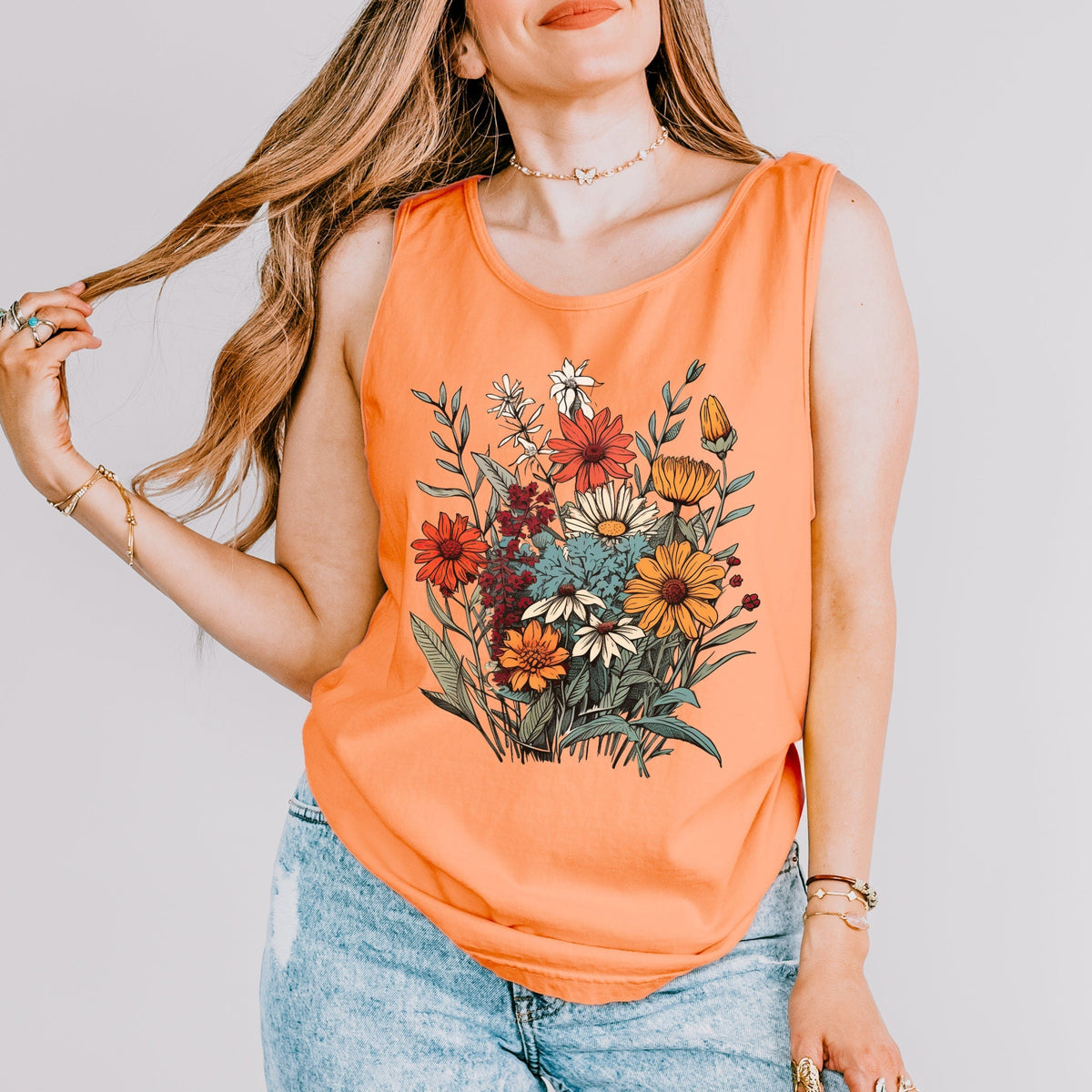 The Faithful Familiar orange slouchy boho tank top with a vintage wildflower graphic, worn by a woman with long hair.