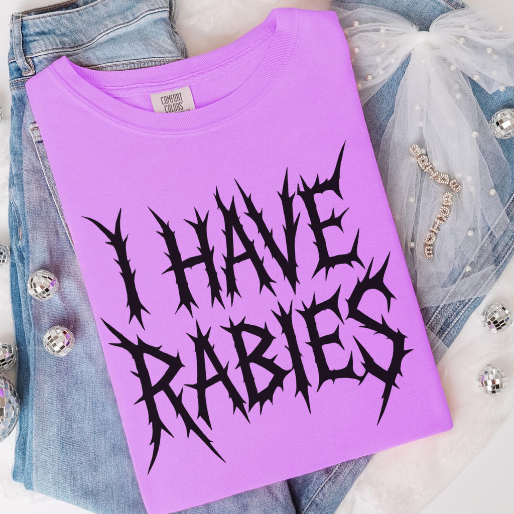 The Faithful Familiar purple Comfort Colors graphic tee with black spiky metal-style text reading I HAVE RABIES.