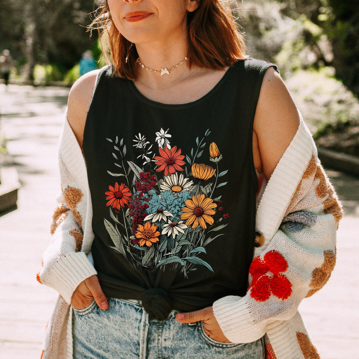 The Faithful Familiar black slouchy boho tank top with a vintage wildflower graphic, worn with a patterned cardigan.